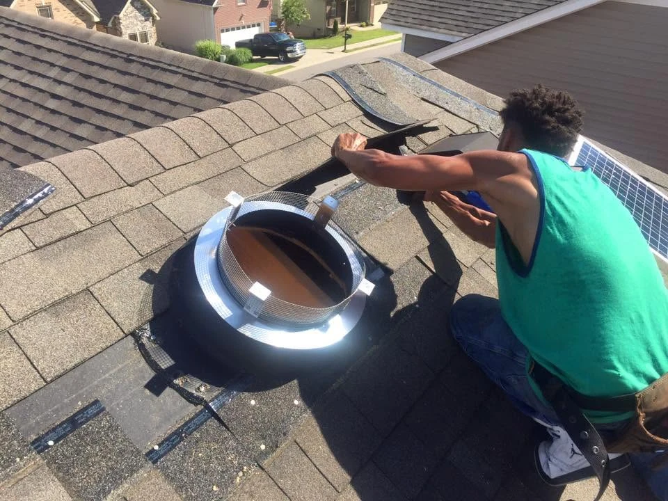 A solar attic fan being installed on a shingle roof